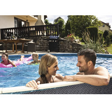 Familie in einem runden Aufstellpool mit grauer Flechtoptik in einem sonnigen Garten mit Terrasse und Grill.
