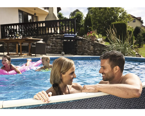 Familie in einem runden Aufstellpool mit grauer Flechtoptik in einem sonnigen Garten mit Terrasse und Grill.