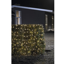 Warmweiß leuchtende LED-Lichterkette für den Außenbereich, um eine Hecke gewickelt, bei Nacht vor einem modernen Haus.