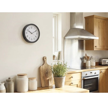Helle Küche mit einer runden Wanduhr an der Wand, Holzschneidebrett, Kräutertopf und Vorratsdosen auf der Arbeitsplatte.