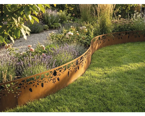 Dekorative Rasenkante aus Metall in Edelrostoptik mit Blumenmuster trennt ein bepflanztes Beet von einer Rasenfläche in einem hellen Garten.