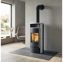Moderner Kaminofen mit brennendem Holzfeuer in einem hellen Wohnzimmer auf einer Schieferplatte vor einer Wand in Betonoptik.