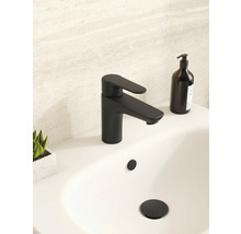 Moderne mattschwarze Waschtischarmatur auf einem weißen Waschbecken in einem hellen Badezimmer mit schwarzem Seifenspender und kleiner Pflanze.
