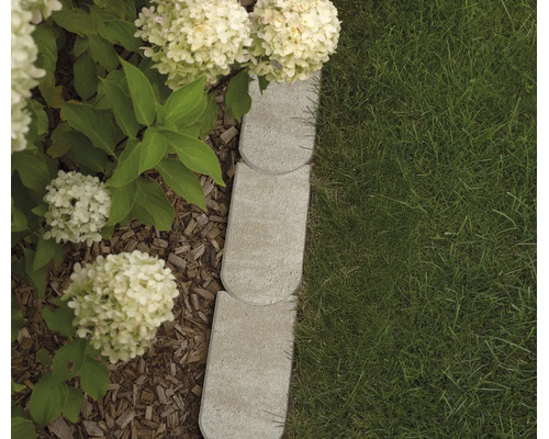 Mähkante aus hellgrauem Beton mit Rundbogenverbindung zwischen Rasen und Beet mit Rindenmulch und weißen Hortensien.