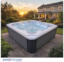Quadratischer Außenwhirlpool mit grauer Verkleidung, sprudelndem Wasser und Beleuchtung auf einer Steinterrasse im Garten. Sanotechnik Logo.
