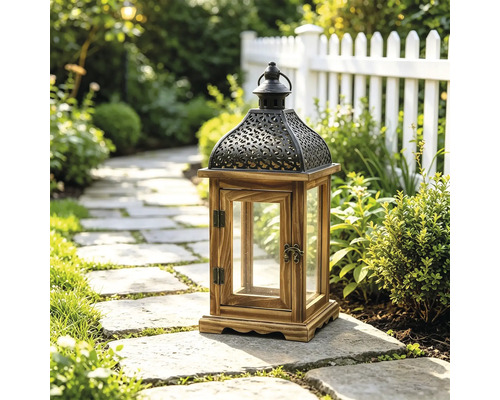 Dekorative Gartenlaterne aus Holz und Metall mit Glaseinsätzen auf einem Steinweg in einem hellen Garten mit Pflanzen und Zaun.