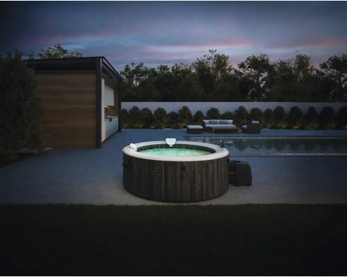 Aufblasbarer Intex Whirlpool in dunkler Holzoptik auf einer modernen Terrasse neben einem Pool bei Dämmerung mit Gartenmöbeln im Hintergrund.