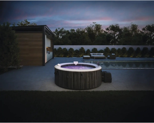 Intex aufblasbarer Whirlpool in Steinoptik auf einer modernen Terrasse mit Pool und Gartenmöbeln bei Abenddämmerung.