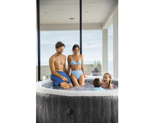 Familie entspannt in einem runden aufblasbaren Whirlpool mit dunkler Holzoptik auf einer hellen Terrasse.
