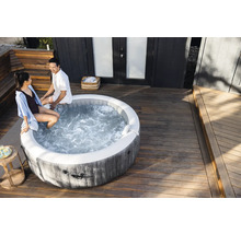Ein runder aufblasbarer Whirlpool in Holzoptik auf einer hellen Holzterrasse mit zwei Personen am Beckenrand.