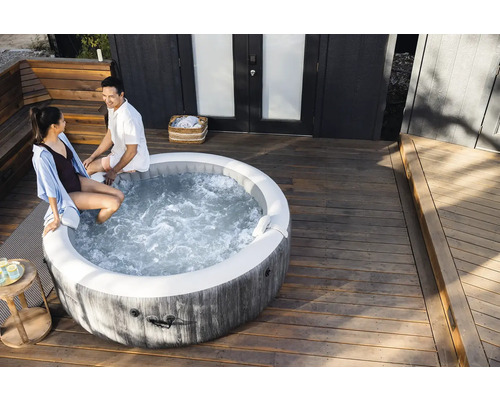 Ein runder aufblasbarer Whirlpool in Holzoptik auf einer hellen Holzterrasse mit zwei Personen am Beckenrand.