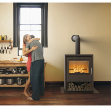 Moderner Kaminofen mit brennendem Feuer und Holzfach in einer hellen Wohnküche mit Holzfußboden und Personen im Hintergrund.
