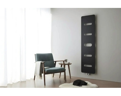 Schwarzer Designheizkörper an grauer Wand in einem hellen Wohnzimmer mit Sessel, Beistelltisch und weißem Teppich.