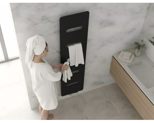 Moderner schwarzer Designheizkörper an einer Marmorwand im Badezimmer mit einer Person im weißen Bademantel und Handtüchern.