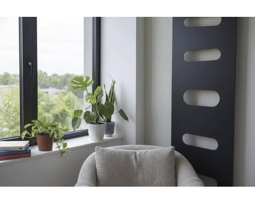 Moderner Innenraum mit schwarzem vertikalem Design-Heizkörper, Zimmerpflanzen am Fenster und grauem Sessel.