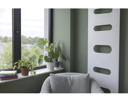 Modernes Wohnzimmer mit salbeigrüner Wand, weißem Design-Heizkörper, Fenster mit Zimmerpflanzen auf der Fensterbank und grauem Sessel.