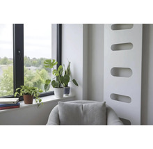 Heller Wohnbereich mit modernem Heizkörper, Sessel und Zimmerpflanzen auf der Fensterbank neben einem Fenster mit schwarzem Rahmen.