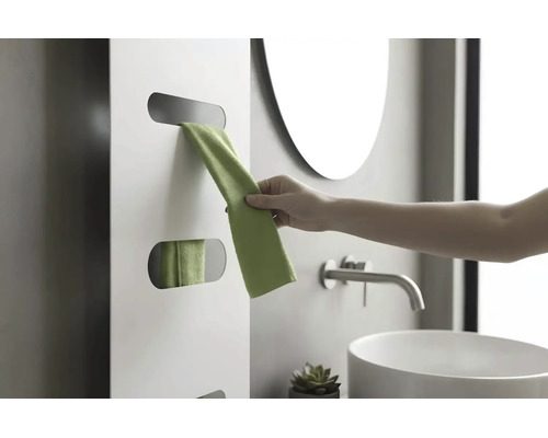 Hand entnimmt ein grünes Handtuch aus einem weißen Design-Heizkörper in einem modernen Badezimmer mit Waschbecken und Armatur.