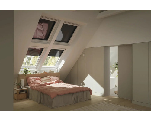 Helles Schlafzimmer im Dachgeschoss mit vier Dachfenstern, Bett mit rosa Bettwäsche, Einbauschränken und Blick in das angrenzende Badezimmer.