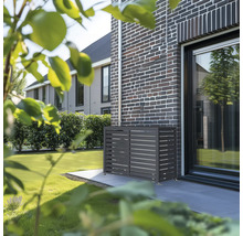 Anthrazitfarbene Wärmepumpen-Verkleidung aus Metall mit horizontalen Lamellen an einer dunklen Klinkerwand im Garten.