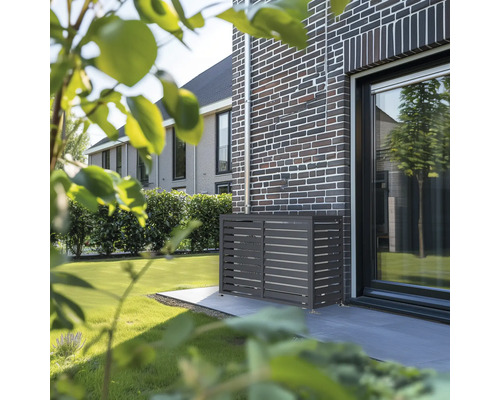 Anthrazitfarbene Wärmepumpen-Verkleidung aus Metall mit horizontalen Lamellen an einer dunklen Klinkerwand im Garten.
