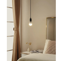 Schlichte Pendelleuchte mit brennendem Leuchtmittel über einem Nachttisch in einem hellen Schlafzimmer mit Vorhängen und Bett.
