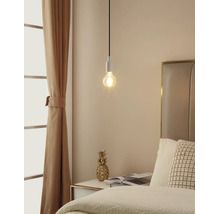 Minimalistische Pendelleuchte mit sichtbarem Leuchtmittel über einem Nachttisch in einem hellen Schlafzimmer mit Bett und Vorhang.