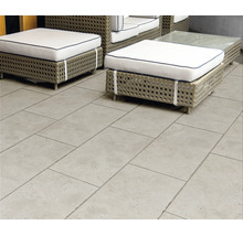 Terrassenplatten in Steinoptik grau auf einer Terrasse mit Gartenmöbeln aus Geflecht und weißen Polstern.