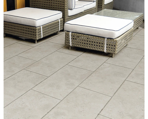 Terrassenplatten in Steinoptik grau auf einer Terrasse mit Gartenmöbeln aus Geflecht und weißen Polstern.