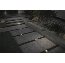 Beleuchteter Gartenweg mit rechteckigen Bodenplatten und quadratischen Bodeneinbaustrahlern in den Zwischenräumen bei Dämmerung.