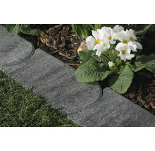 Anthrazitfarbene Rasenkante aus Beton trennt eine Rasenfläche von einem Beet mit Rindenmulch und weißen Primeln.