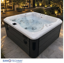 Quadratischer Außenwhirlpool mit dunkler Verkleidung auf einer beleuchteten Terrasse im Garten. Sanotechnik International Logo.
