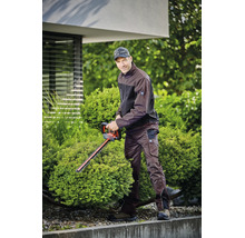 Ein Mann in brauner Arbeitsjacke und Arbeitshose schneidet einen runden Strauch mit einer Heckenschere im Garten.