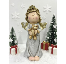Helle Weihnachtsdekoration mit einem Engel mit goldenen Flügeln, der einen Teddybär hält, zwischen Tannenbäumen und Geschenken auf Kunstschnee.