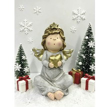Festliche Szene mit einer sitzenden Engelsfigur, die ein Herz hält, umgeben von kleinen Weihnachtsbäumen, Geschenken und Schneeflocken auf Kunstschnee.