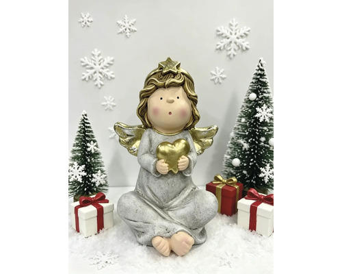 Festliche Szene mit einer sitzenden Engelsfigur, die ein Herz hält, umgeben von kleinen Weihnachtsbäumen, Geschenken und Schneeflocken auf Kunstschnee.