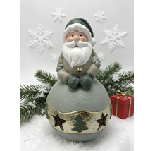 Weihnachtsmann Dekofigur auf einer Kugel mit Sternen und Tannenbaum Aussparungen, Tannenzweige und Geschenk im Hintergrund.