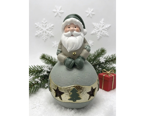 Weihnachtsmann Dekofigur auf einer Kugel mit Sternen und Tannenbaum Aussparungen, Tannenzweige und Geschenk im Hintergrund.
