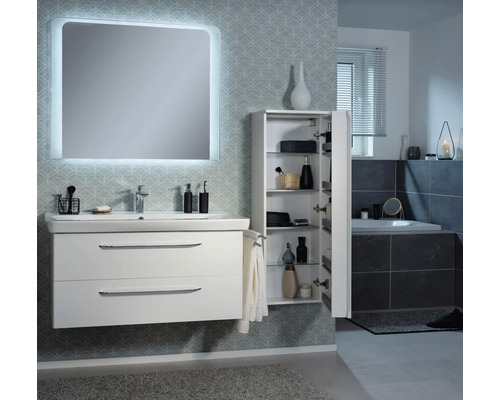 Modernes Badezimmer mit weißem Waschtischunterschrank, beleuchtetem Spiegel und geöffnetem Hochschrank mit Glasböden vor gemusterter Tapete.