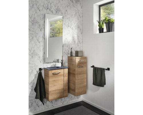 Modernes Badezimmer mit Waschtischunterschrank und Beischrank in Holzoptik vor einer Wand in Marmoroptik mit beleuchtetem Spiegel.