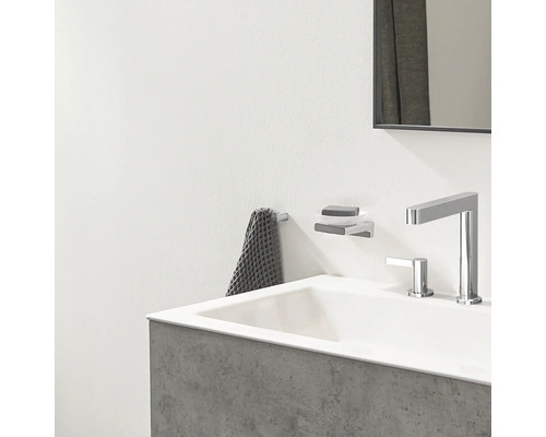 Modernes Badezimmer mit weißem Waschbecken, verchromter Armatur, Seifenhalter zur Wandmontage und grauem Handtuch an einem Haken.