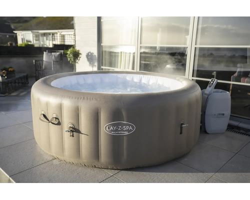 Runder, aufblasbarer Whirlpool Lay-Z-Spa Palm Springs auf einer Fliesenterrasse vor einer Glasfront mit dampfendem Wasser.