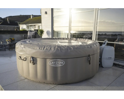 Aufblasbarer Whirlpool Lay-Z-Spa Palm Springs mit Abdeckung und Steuereinheit auf einer hellen Terrasse vor einer Glasfront.