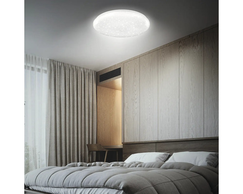 Moderne LED-Deckenleuchte mit Sternenhimmel-Effekt in einem hellen Schlafzimmer mit Holzwand und grauen Textilien.