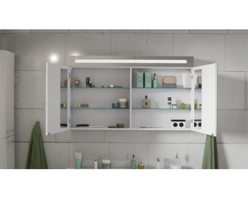 Spiegelschrank für das Bad mit LED-Beleuchtung, zwei offenen Türen, Glaseinlegeböden und Steckdose, befüllt mit Kosmetik vor einer Fliesenwand.