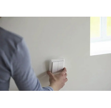 Person montiert einen weißen Doppel-Lichtschalter an einer Wand in einem hellen, modern gestalteten Raum.