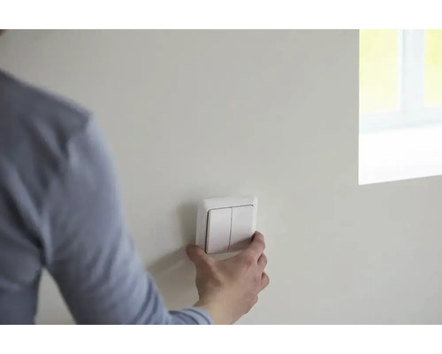 Person montiert einen weißen Doppel-Lichtschalter an einer Wand in einem hellen, modern gestalteten Raum.