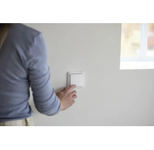 Hand betätigt einen weißen Lichtschalter in einem hellen, modern gestalteten Raum.