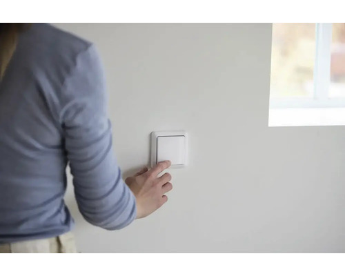 Hand betätigt einen weißen Lichtschalter in einem hellen, modern gestalteten Raum.