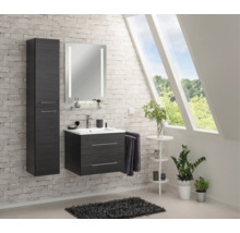 Modernes Badezimmer-Set in Holzoptik mit Waschtischunterschrank, Hochschrank und beleuchtetem Spiegel an einer Backsteinwand.